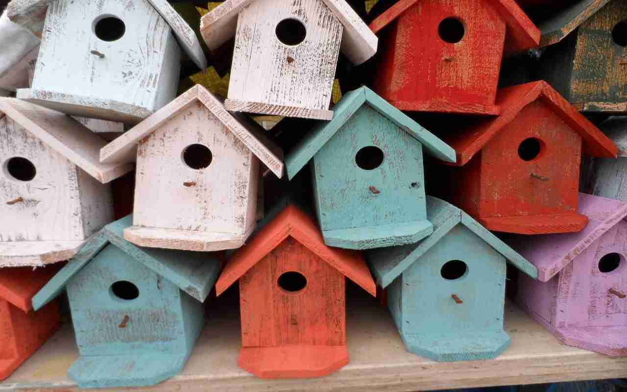 A collection of 12 birdhouses in a garden, featuring shades of red, blue, white, and violet, demonstrating what colors attract birds.