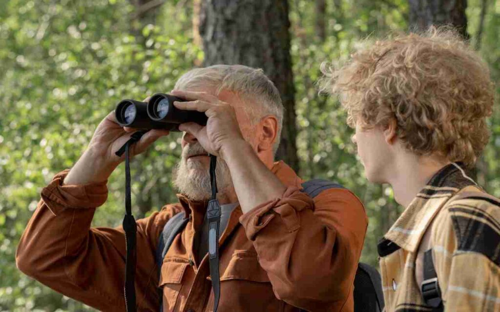 A senior man birdwatching with high-quality lightweight binoculars alongside a younger person.