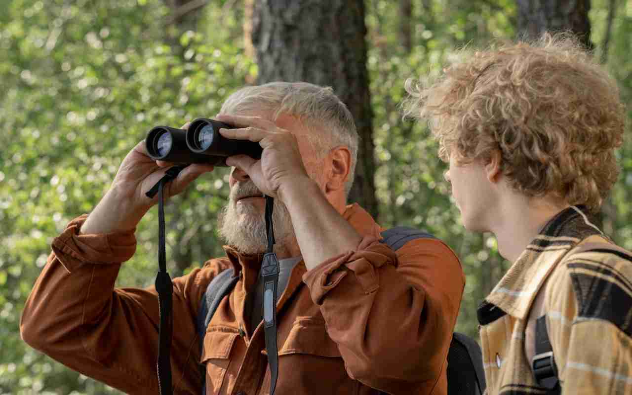 A senior man birdwatching with high-quality lightweight binoculars alongside a younger person.