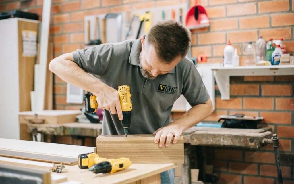 A man in a workshop using a yellow power drill to bore a precise hole into a block of wood.